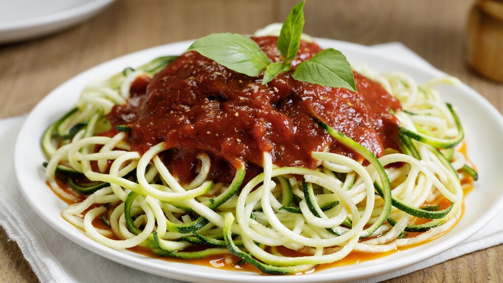 Zucchini noodles topped with marinara sauce and fresh basil on a white plate.