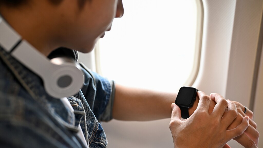 Traveler checking a smartwatch during a flight, suggesting time-zone planning for diabetes medication routines.
