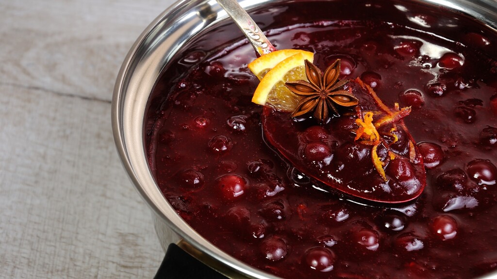 Thick berry sauce simmering in a saucepan with a spoon, citrus peel, and warm spices.