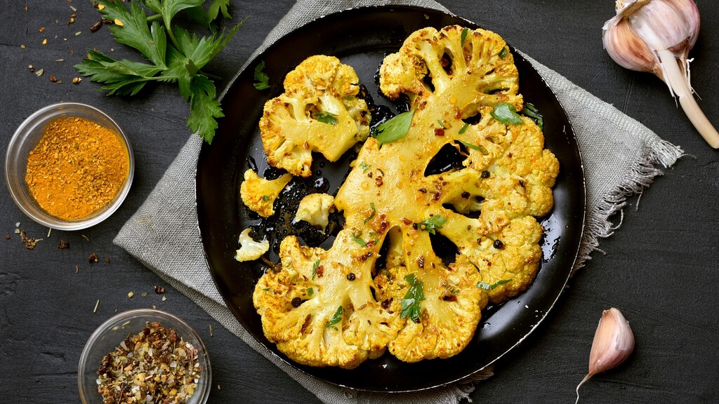 Roasted cauliflower steaks seasoned with spices and herbs, served on a black plate with garlic and parsley.