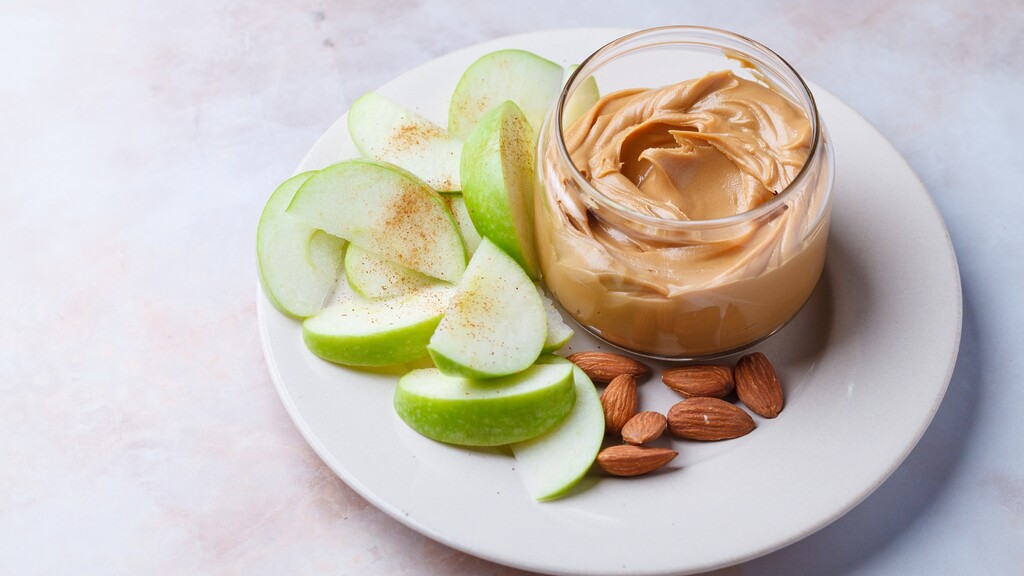 Apple slices served with peanut butter and almonds on a plate.