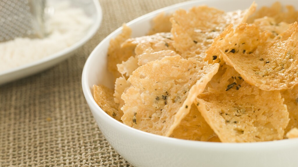 Bowl of baked cheese crisps with herbs, served beside a small dish of creamy dip.