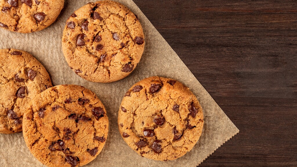 Chocolate chip cookies on parchment paper over a dark wooden table.