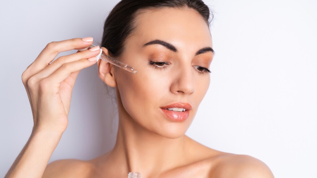 Woman using a dropper serum on her face for gentle chemical exfoliation and skin hydration.