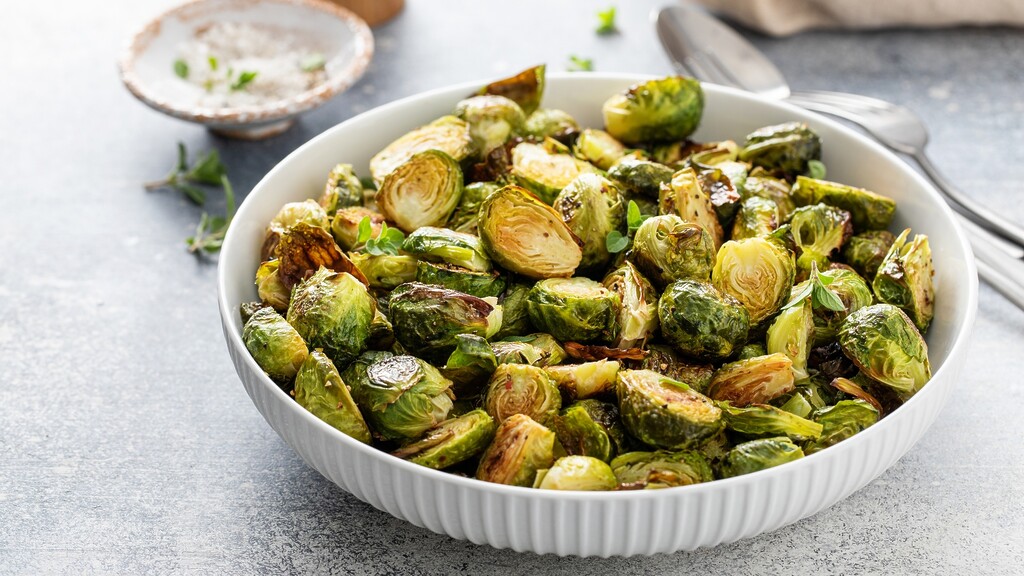Roasted Brussels sprouts in a white bowl, garnished with herbs and served on a light gray tabletop.