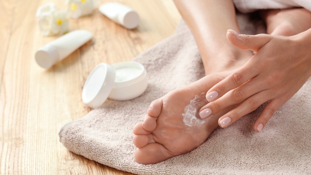 Woman applying thick foot cream to her heel to soften dry, rough skin.