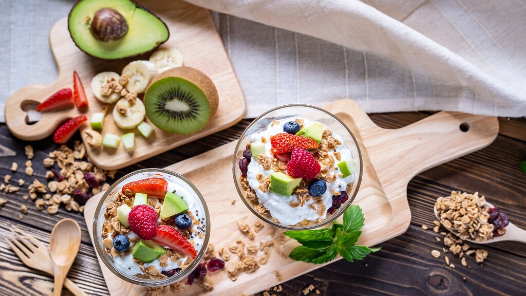 Greek yogurt parfaits with berries, avocado, granola, and fresh fruit on wooden boards.
