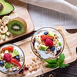 Greek yogurt parfaits with berries, avocado, granola, and fresh fruit on wooden boards.