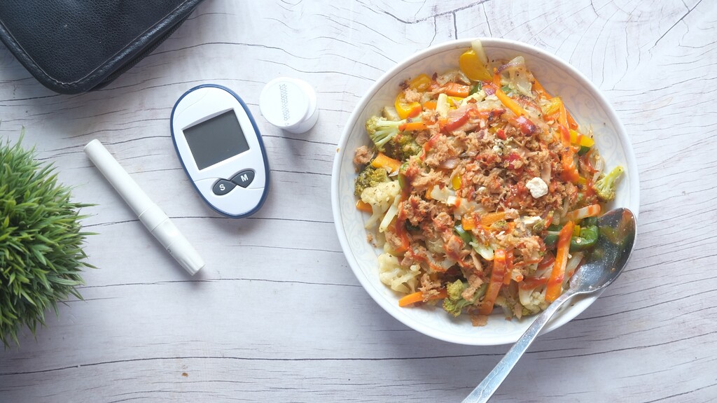 Blood glucose meter beside a bowl of vegetables and protein, representing diabetes-friendly meal planning.