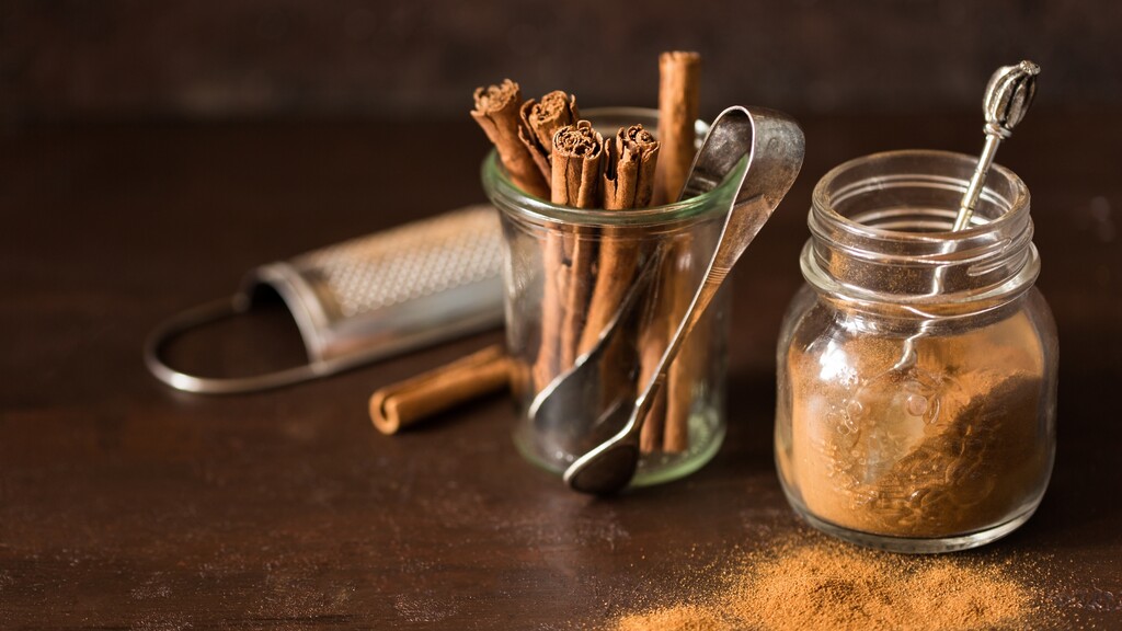 Cinnamon sticks and ground cinnamon in glass jars on a dark wooden table.