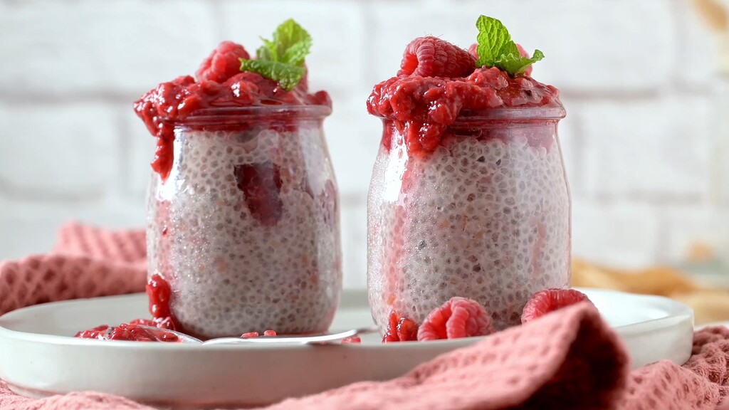 Chia seed pudding in glass jars topped with raspberry compote and fresh raspberries.