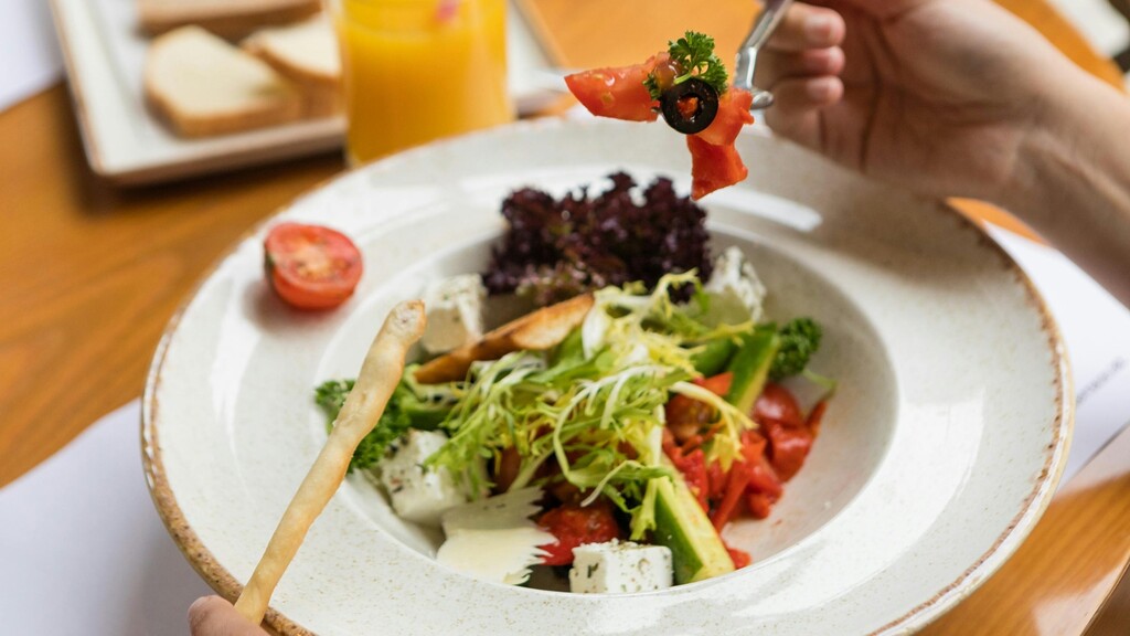 Person eating a vegetable salad first, with bread in the background, illustrating meal order for blood sugar control.