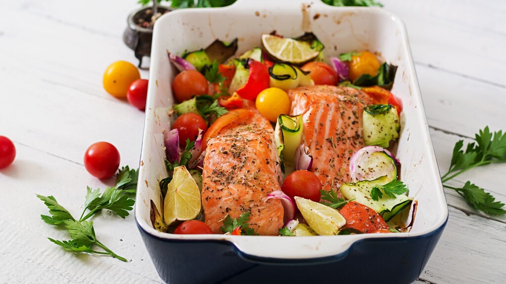 Baked salmon fillets with vegetables, lemon wedges, and fresh herbs in a roasting dish.
