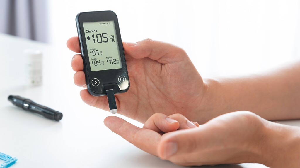 Person holding a blood glucose meter showing a reading of 105 mg/dL.