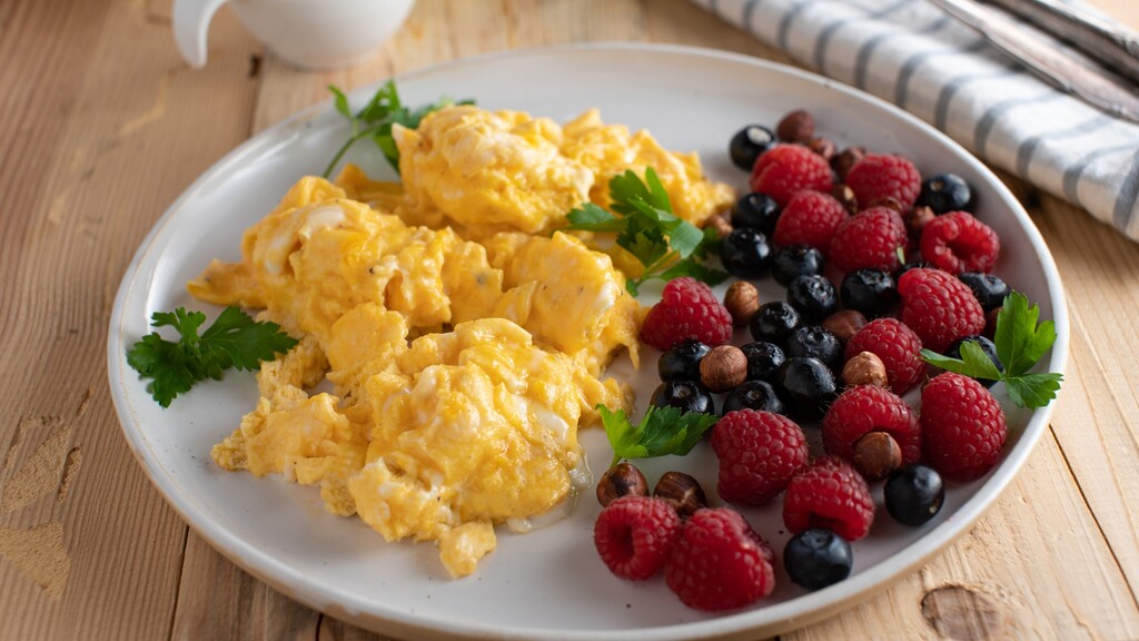 Plate of scrambled eggs with berries and nuts, showing a protein-rich breakfast with fruit.