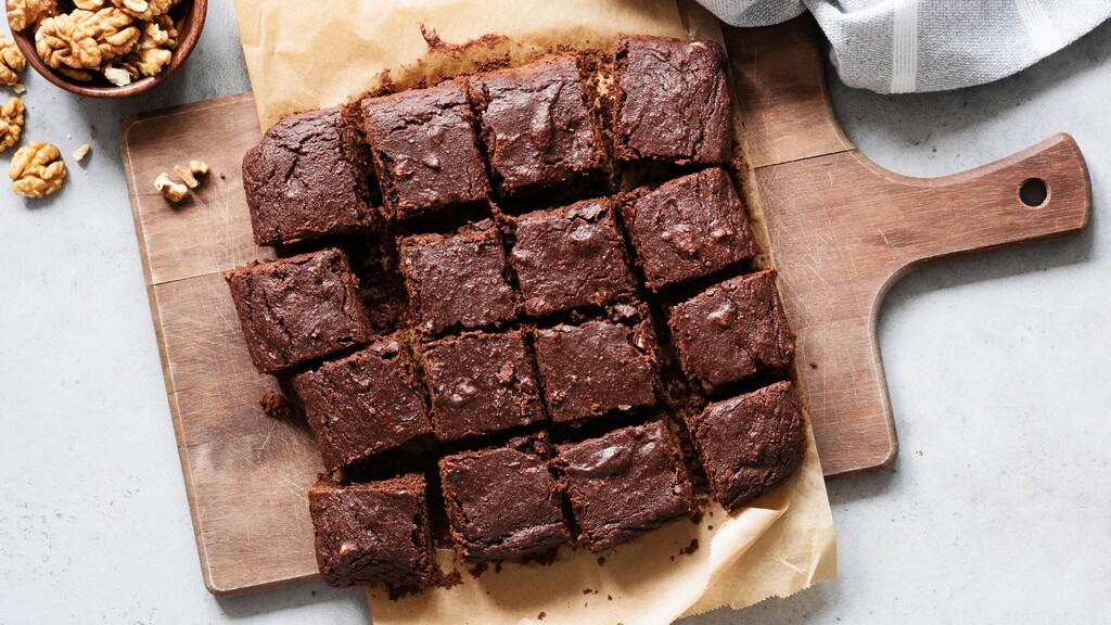 Sliced chocolate brownies on parchment paper, served on a wooden cutting board with walnuts nearby.
