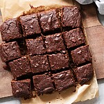 Sliced chocolate brownies on parchment paper, served on a wooden cutting board with walnuts nearby.