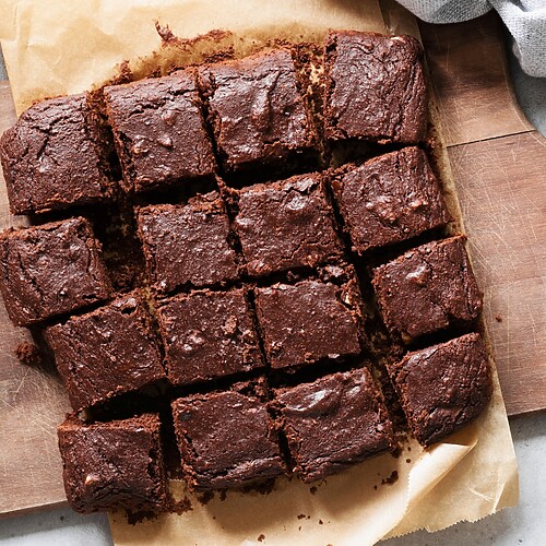 Sliced chocolate brownies on parchment paper, served on a wooden cutting board with walnuts nearby.