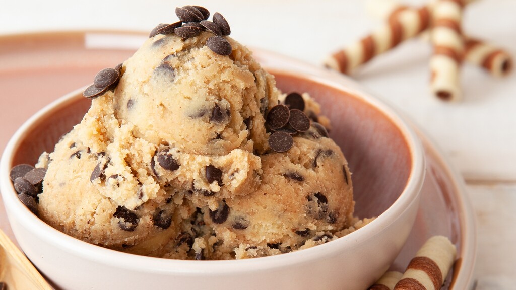 Bowl of edible cookie dough with chocolate chips, served with wafer rolls in the background.