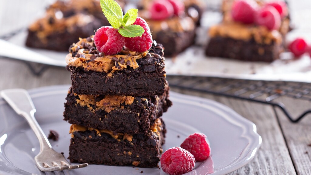 Stacked chocolate peanut butter brownies topped with raspberries and mint on a dessert plate.