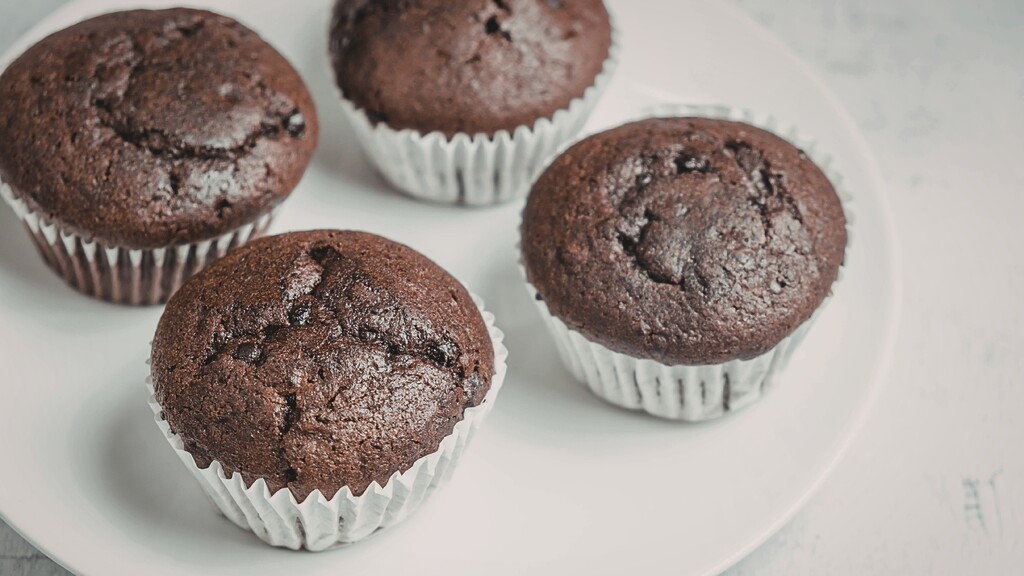 Chocolate protein muffins in paper liners arranged on a white plate.