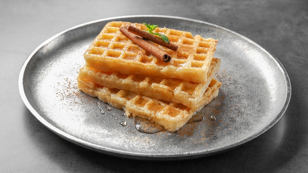 Crispy waffles topped with cinnamon and syrup on a gray plate.