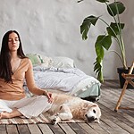 Woman meditating on a rug beside a relaxed dog in a peaceful bedroom.
