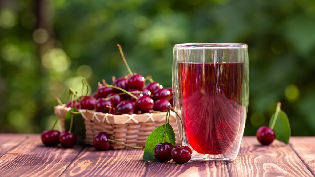 Tart cherry juice in a glass beside fresh cherries on a wooden table.