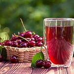 Tart cherry juice in a glass beside fresh cherries on a wooden table.