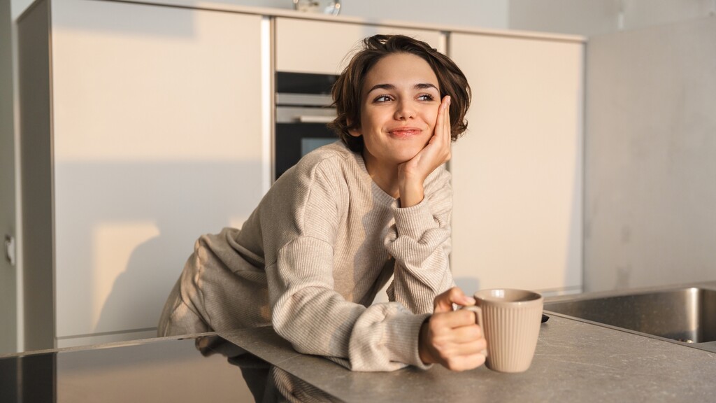 Woman holding a coffee mug in a quiet kitchen, taking a calm morning moment before starting the day.