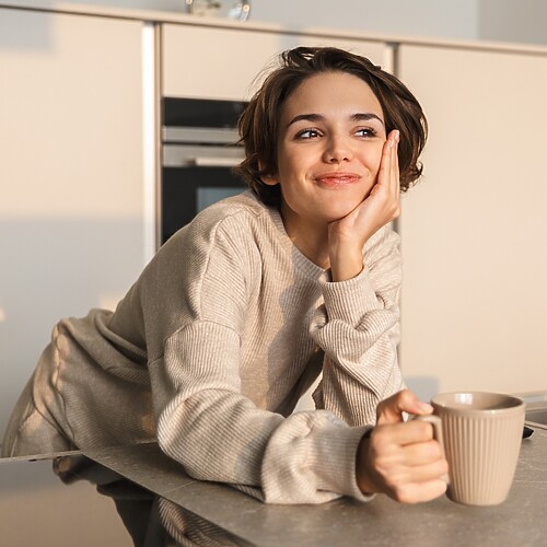 Woman holding a coffee mug in a quiet kitchen, taking a calm morning moment before starting the day.