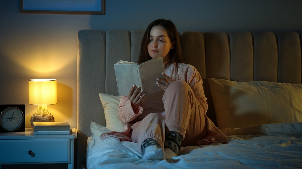 Woman reading in bed beside a warm bedside lamp as part of a calming bedtime routine.