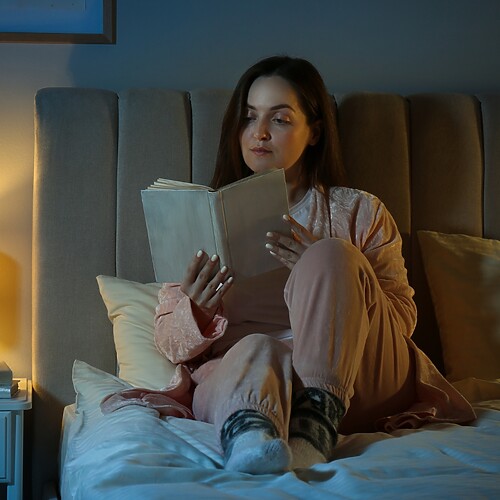 Woman reading in bed beside a warm bedside lamp as part of a calming bedtime routine.