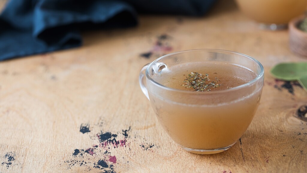A warm cup of bone broth with herbs on a wooden table.