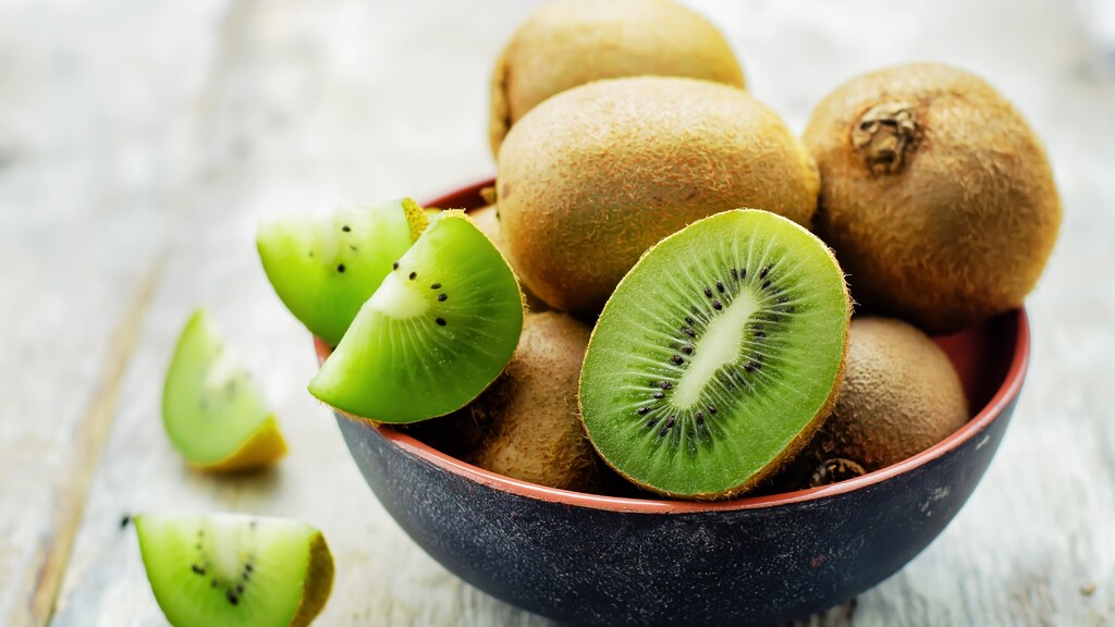 Fresh kiwi fruits, including one sliced open, arranged in a dark bowl.