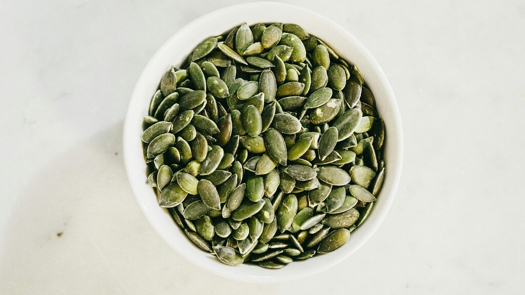 Roasted pumpkin seeds in a small white bowl on a light surface.