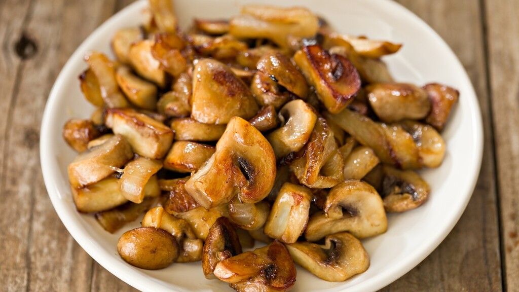 Sautéed mushrooms served on a white plate over a wooden table.
