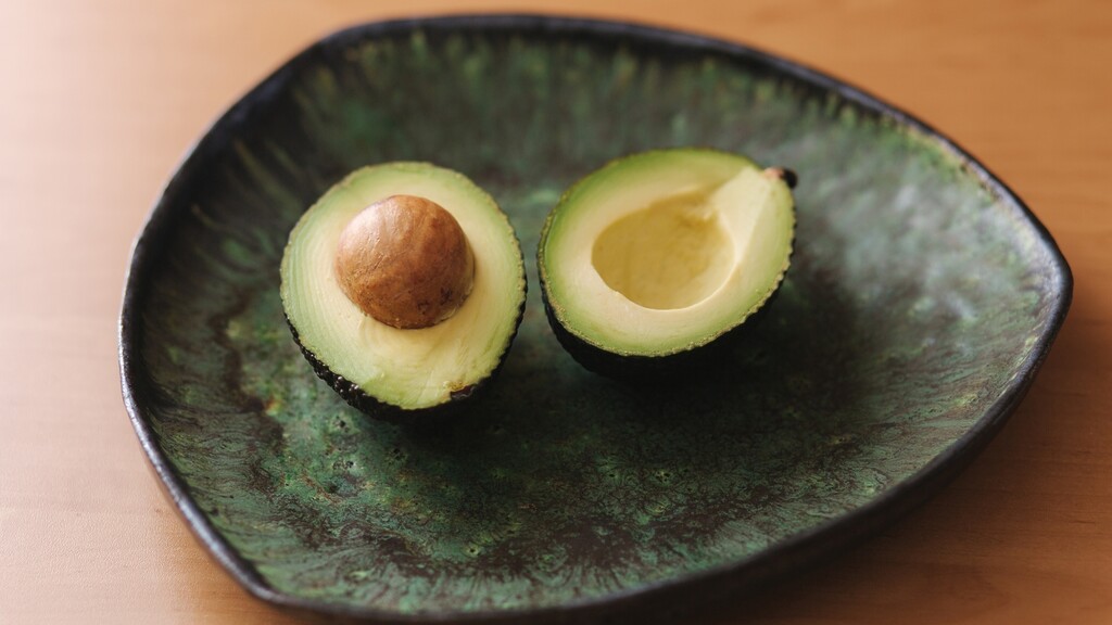 Two avocado halves served on a green ceramic plate.