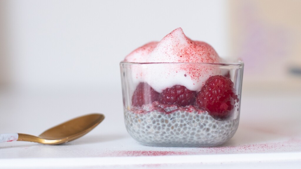Chia seed pudding topped with raspberries in a small glass cup.