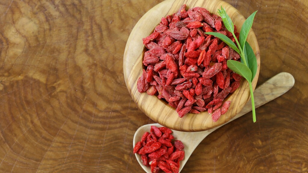 Dried goji berries in a wooden bowl with a small spoon on a rustic table.