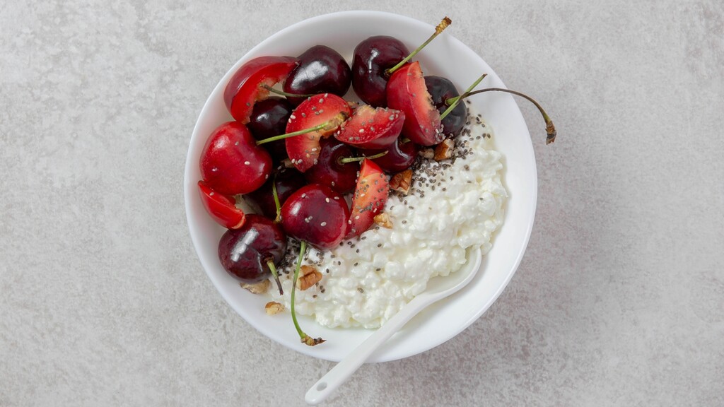 Cottage cheese topped with tart cherries, chia seeds, and walnuts in a white bowl.
