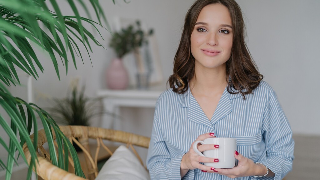 Woman in blue striped pajamas holding a white mug in a calm home setting with indoor plants.