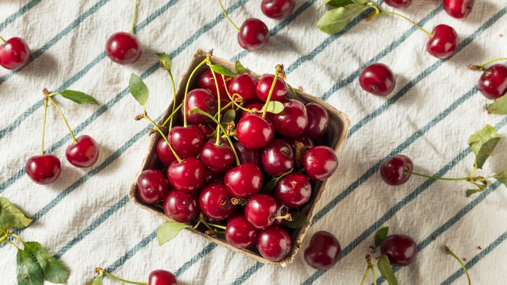 Fresh red cherries in a carton on a striped kitchen towel.
