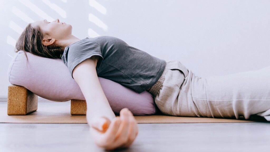 Woman lying on a yoga bolster with eyes closed during a body scan meditation.
