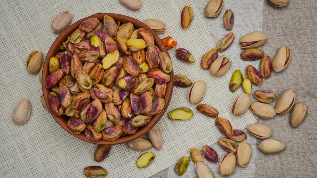 Bowl of shelled pistachios with scattered pistachio nuts on a textured cloth background