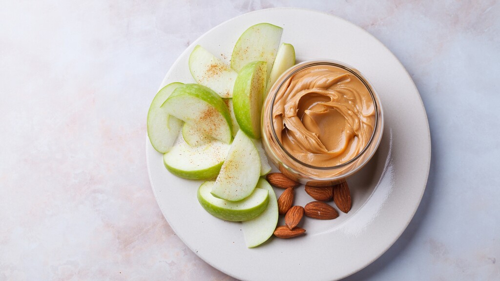 Green apple slices served with almond butter and almonds on a white plate.