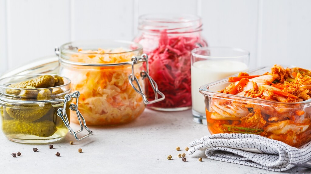 Fermented foods including kimchi, sauerkraut, pickles, and kefir arranged on a light kitchen surface.
