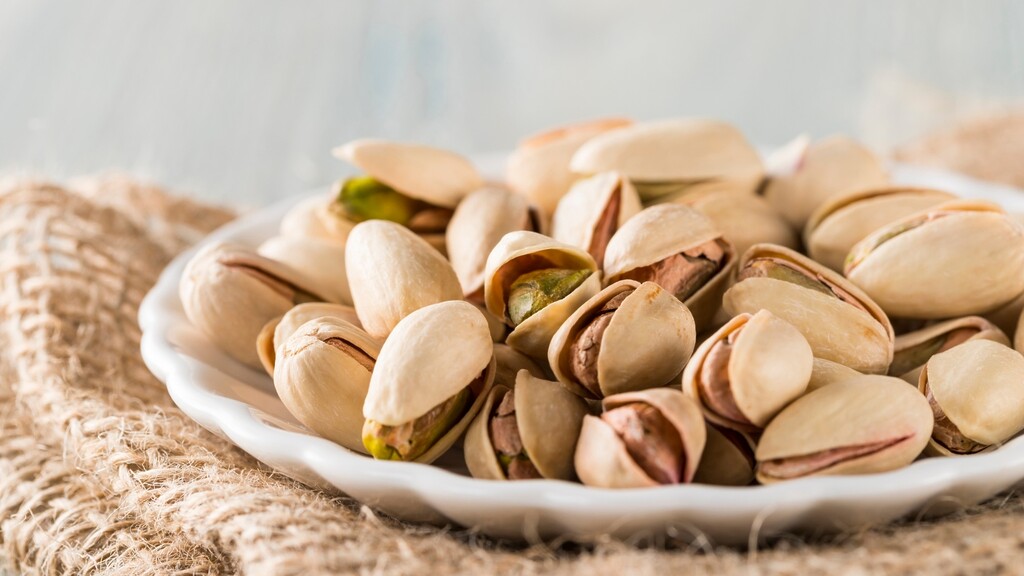 Roasted pistachios piled on a white plate over a burlap cloth.