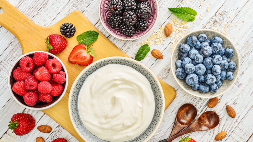 Greek yogurt with fresh raspberries, blueberries, strawberries, blackberries, almonds, oats, and mint on a wooden board