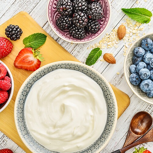 Greek yogurt with fresh raspberries, blueberries, strawberries, blackberries, almonds, oats, and mint on a wooden board